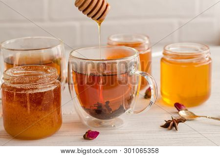 A Viscous Stream Of Sweet Amber Flower Honey Flows From A Wooden Honey Spoon Into A Glass Cup Of Tea