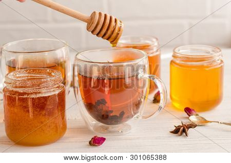 A Viscous Stream Of Sweet Amber Flower Honey Flows From A Wooden Honey Spoon Into A Glass Cup Of Tea