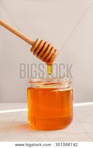 A Viscous Stream Of Sweet Amber Flower Honey Flows From A Wooden Honey Spoon Into A Glass Jar.