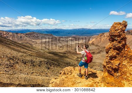 New Zealand Tongariro Alpine Crossing hike trail nature landscape hiker man taking picture of background. Happy tramper filming phone photo at volcanic mountains . Summer adventure Travel.