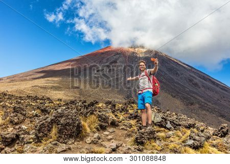 Hiking man on New Zealand Travel taking selfie at Tongariro Alpine Crossing hike trail. Happy hiker tramper phone photo of himself at volcanic mountains background. Summer adventure.