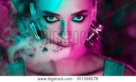 Smoking E-cigarette. Woman In Green And Pink Neon Lights, Looking At Camera