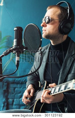 Close Up Of A Man Singer Sitting On A Stool In A Headphones With A Guitar Recording A Track In A Hom