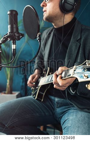 Close Up Of A Man Singer Sitting On A Stool In A Headphones With A Guitar Recording A Track In A Hom