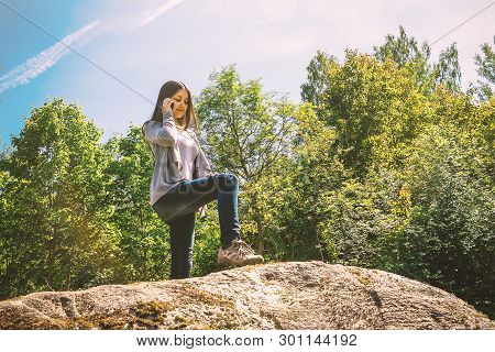 Young Pretty Girl Smiles And Talks On The Phone While Standing On A Large Stone