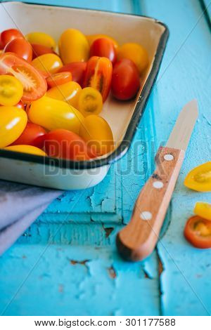 Small Cherry Tomatoes, Red And Yellow, In An Enameled Baking Sheet On A Blue Background