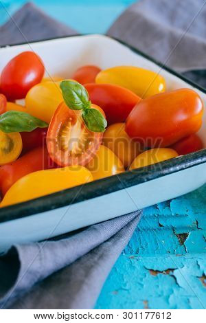 Small Cherry Tomatoes, Red And Yellow, In An Enameled Baking Sheet On A Blue Background