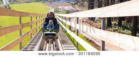 Excited young father and son driving on alpine coaster while enjoying beautiful sunny day in the nature