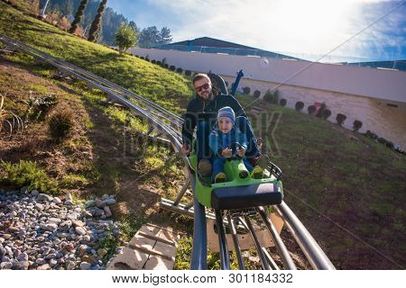 Excited young father and son driving on alpine coaster while enjoying beautiful sunny day in the nature