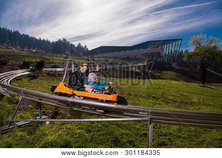 Excited young mother and son driving on alpine coaster while enjoying beautiful sunny day in the nature