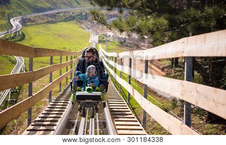 Excited young father and son driving on alpine coaster while enjoying beautiful sunny day in the nature