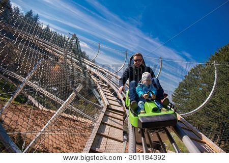 Excited young father and son driving on alpine coaster while enjoying beautiful sunny day in the nature