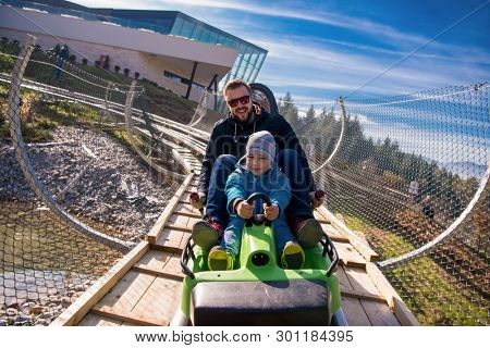 Excited young father and son driving on alpine coaster while enjoying beautiful sunny day in the nature