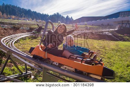 Excited young mother and son driving on alpine coaster while enjoying beautiful sunny day in the nature