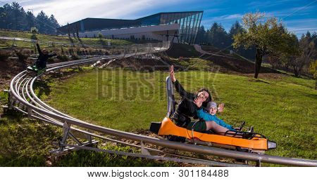 Excited young mother and son driving on alpine coaster while enjoying beautiful sunny day in the nature
