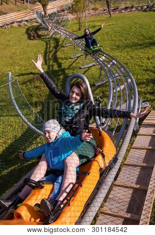 Excited young mother and son driving on alpine coaster while enjoying beautiful sunny day in the nature