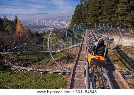 Excited young mother and son driving on alpine coaster while enjoying beautiful sunny day in the nature