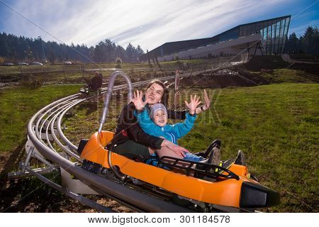 Excited young mother and son driving on alpine coaster while enjoying beautiful sunny day in the nature