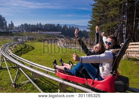 Excited young couple driving alpine coaster while enjoying beautiful sunny day in the nature