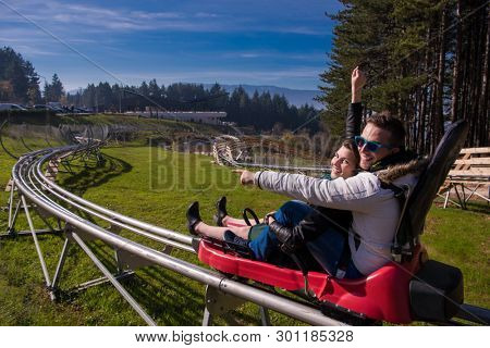 Excited young couple driving alpine coaster while enjoying beautiful sunny day in the nature