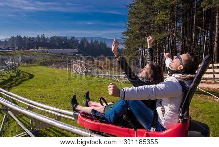 Excited young couple driving alpine coaster while enjoying beautiful sunny day in the nature