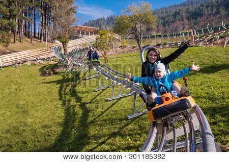 Excited young mother and son driving on alpine coaster while enjoying beautiful sunny day in the nature