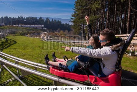 Excited young couple driving alpine coaster while enjoying beautiful sunny day in the nature