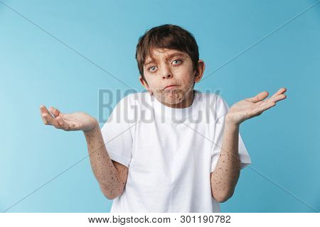 Image closeup of surprised caucasian boy 10-12y with freckles wearing white casual t-shirt smiling at camera isolated over blue background