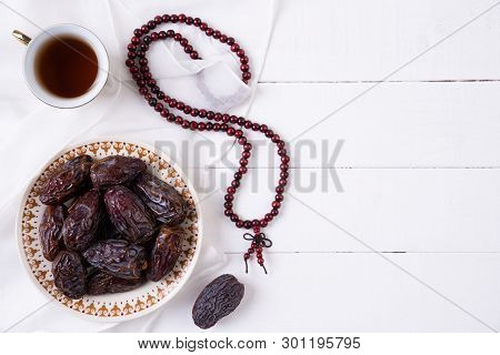 Ramadan Food And Drinks Concept. Wood Rosary, Tea And Dates Fruit On A White Wooden Table Background
