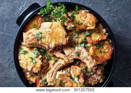 Delicious Browned Pork Chops On Bone And Hash Brown Casserole In A Black Ceramic Pan On A Concrete T