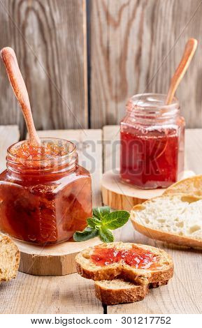 Two Glass Jars Of Strawberry And Apple Jam And Sliced Bread On Wooden Background.