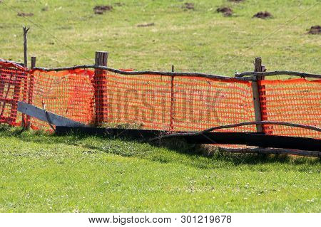 Bright Orange Makeshift Improvised Fence Made Of Nylon Net And Wooden Poles Surrounded With Uncut Gr