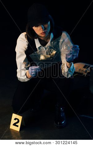 Investigator In Rubber Gloves Holding Ziploc Bag With Dollar Banknote At Crime Scene