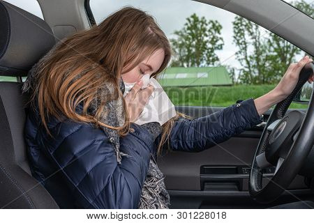 A Young Woman Sneezes While Driving Car In A Handkerchief