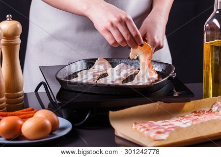 Young Woman In A Gray Apron Fries Bacon