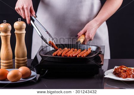 Young Woman In A Gray Apron Fries Sausages