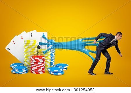 Young Businessman Stuck To Playing Cards And Casino Chips With Blue Sticky Slime On Yellow Backgroun
