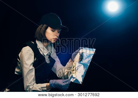 Investigator In Rubber Gloves Holding Ziploc Bag With Dollar Banknote At Crime Scene