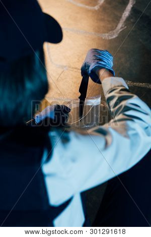 Selective Focus Of Investigator Putting Knife In Ziploc Bag At Crime Scene