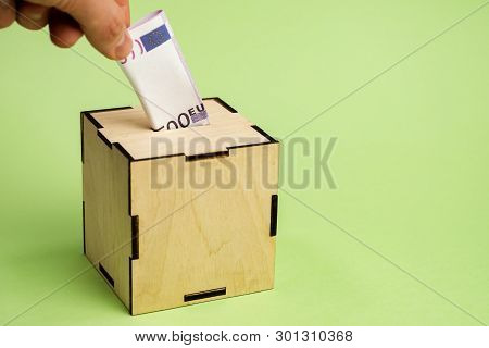Hand Depositing Euro Bill Into Moneybox On The Green Background.