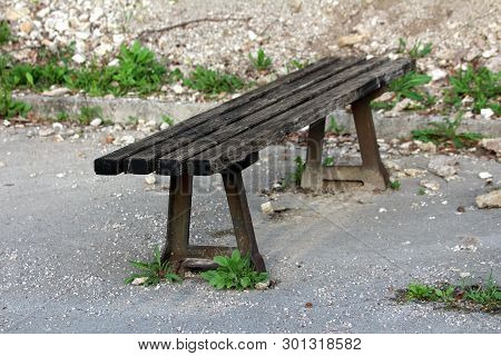 Old Wooden Public Bench With Strong Rusted Metal Supports Mounted On Paved Edge Of Abandoned Parking