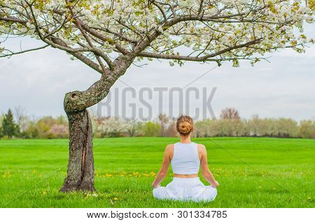 Meditation. Woman Is Meditating Sitting In Lotus Pose On Grass At The Park. Girl Doing Ardha Padmasa