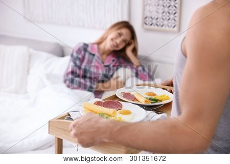 Young handsome man bringing breakfast for his beloved girlfriend in bed