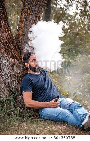 Bearded Vape Man Blows Up A Couple An Vape In The Woods. Hybrid Cigarette.