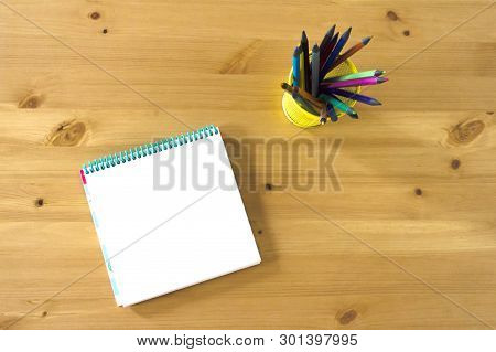 Notebook Sketch Book And Glass With Pencils And Pens On A Wooden Table. View From Above