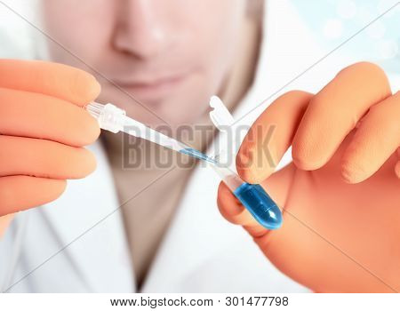 Male Scientist In Protective Wear And Orange Gloves Loads Blue Liquid Sample. Shallow Dof, Focus On 