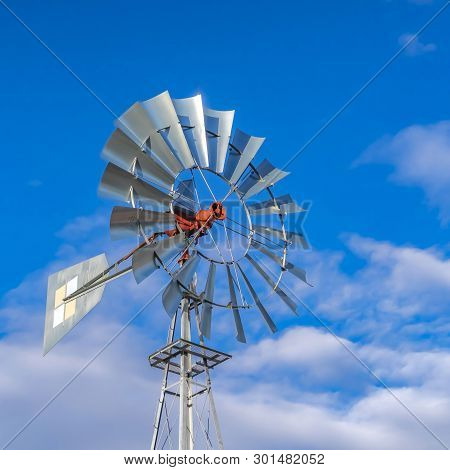 Square Shiny Steel Windpump Against A Vibrant Blue Sky With Cottony Clouds