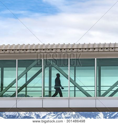 Square Silhouette Of A Man Walking Inside A Skybridge Connecting Buildings