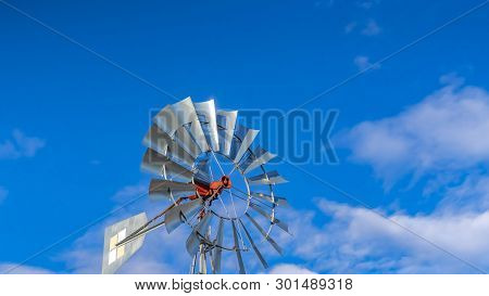 Panorama Shiny Steel Windpump Against A Vibrant Blue Sky With Cottony Clouds