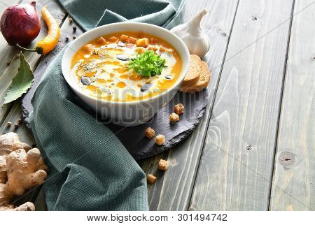 Spicy Pumpkin Soup With Chili And Garlic, Served With Cream, Pumpkin Seeds And Parsley. Wooden Backg